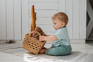 Nane rengi elbiseli çocuk mutfakta bir sepet taze ekmekle oturuyor.