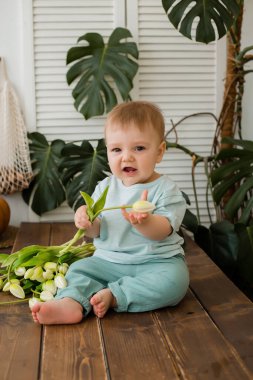 Ufaklık mutfakta masada oturuyor ve arkasında laleler ve canavarlar var.