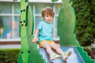 İki yıllık mavi tişörtlü kızıl saçlı sevimli çocuk oyun parkında kayarken eğleniyor. Çocuk yaşam tarzı konsepti