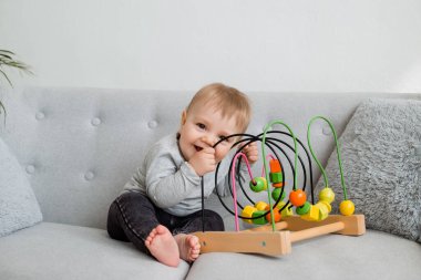 Küçük çocuk evdeki gri kanepede otururken gelişim oyunu oynuyor. 