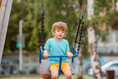 2 yıllık tatlı kızıl çocuk, çocuk parkında salıncakta sallanırken eğleniyor.