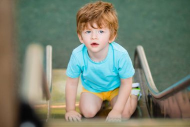 İki yıllık mavi tişörtlü kızıl saçlı sevimli çocuk oyun parkında kayarken eğleniyor. Çocuk yaşam tarzı konsepti