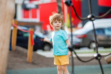Mavi tişörtlü küçük çocuk oyun parkının dışında vakit geçiriyor.