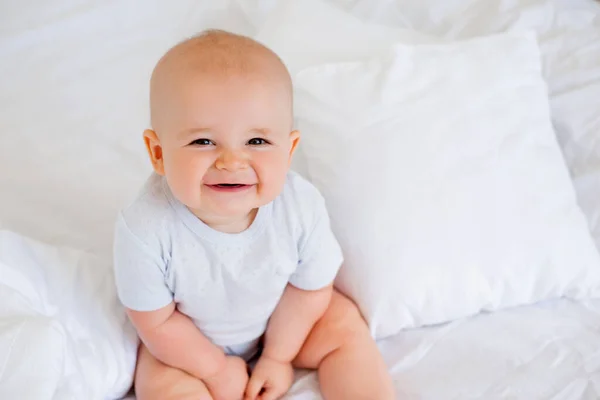 照片上是一个快乐的6个月大的男婴 穿着白色的紧身衣躺在床上 — 图库照片