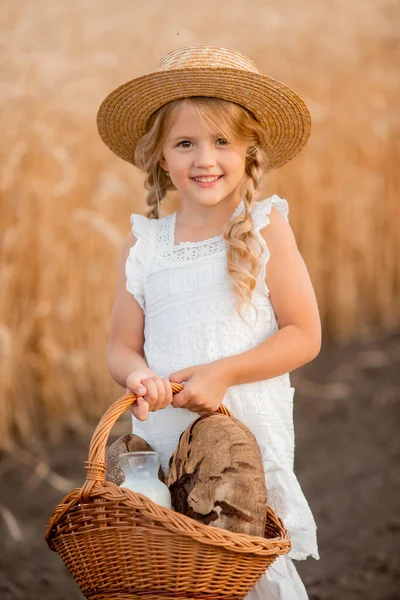 Buğday tarlasında elinde bir sepet ev ekmeği olan küçük sarışın bir kız. Çevre dostu eko tarım ürünleri kavramı.