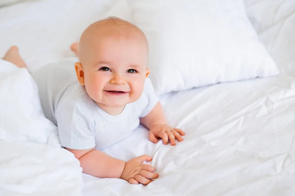 照片上是一个快乐的6个月大的男婴 穿着白色的紧身衣躺在床上 — 图库照片