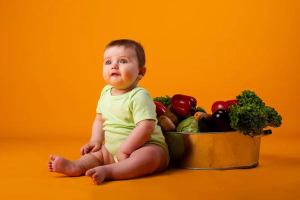 赤ちゃんの少年は 新鮮な野菜 環境に優しい農産物の概念を持つ大きなボウルの横に座っている オレンジの背景に孤立した画像 — ストック写真