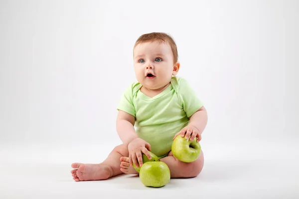 緑のボディスーツのかわいい幼児が座って緑のリンゴで遊んでいます 白い背景に孤立したイメージ — ストック写真