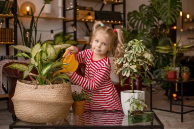 Şirin küçük kız annesinin güzel dairesinde çiçeklerini sulamasına yardım ediyor..