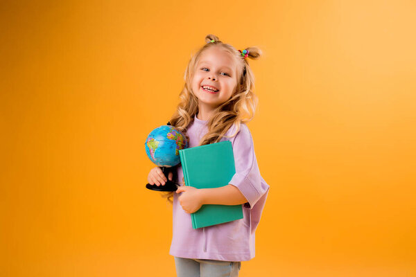 Веселая блондинка с глобусом и книгой в руках. Isolated on orange background, children 's emotions and back to school concept. 