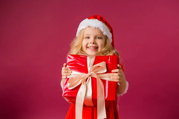 Kleines Blondes Mädchen Weihnachtsmannkostüm Mit Großer Geschenkbox Auf Rotem Hintergrund — Stockfoto