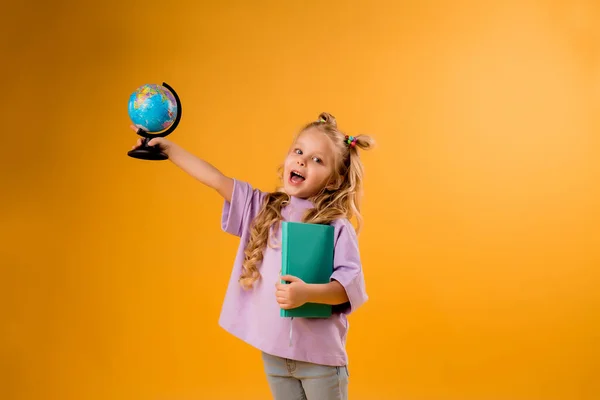 Wesoła Blondynka Trzymająca Kulę Księgę Rękach Odizolowane Pomarańczowym Tle Dziecięce — Zdjęcie stockowe