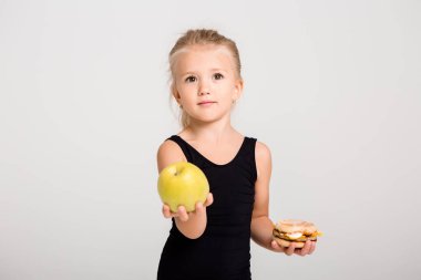 Gülümseyen kız bir elma ve bir hamburger tutuyor. Sağlıklı yemek seçiyorum, fast food yok, yazı için yer var.