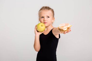 Gülümseyen kız bir elma ve bir hamburger tutuyor. Sağlıklı yemek seçiyorum, fast food yok, yazı için yer var.