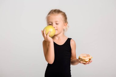 Gülümseyen kız bir elma ve bir hamburger tutuyor. Sağlıklı yemek seçiyorum, fast food yok, yazı için yer var.