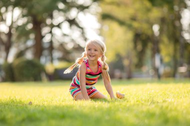 Açık havada oynayan, renkli elbiseli, sevimli sarışın küçük kız. 