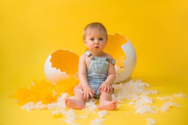 Bebek sarı arka planda dekoratif paskalya yumurtalarıyla oturuyor. Paskalya konsepti