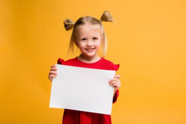 Sarı arka planda beyaz bir çarşaf tutan bir kızın fotoğrafı. Reklam metniniz için boşluk resmini yerleştirerek kopyalayın