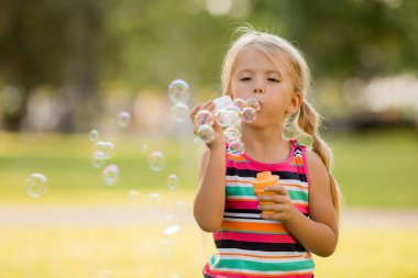 Açık havada oynayan, renkli elbiseli, sevimli sarışın küçük kız. 