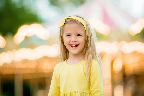 happy blond little girl in yellow dress in amusement park