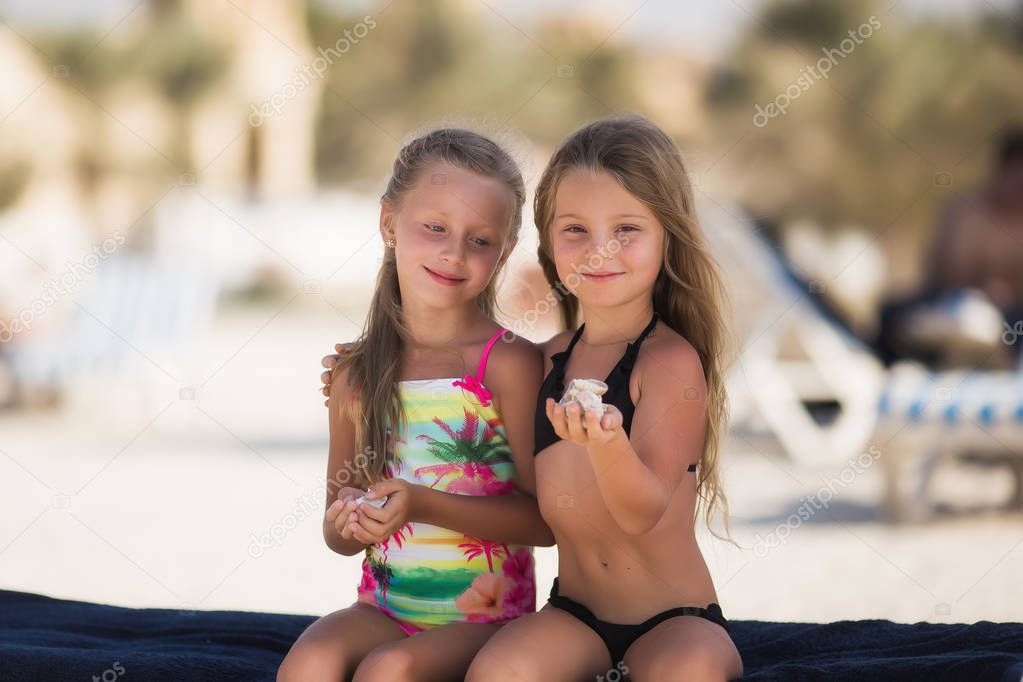 Two beautiful happy girl on the beach near the sea with shells in their hands