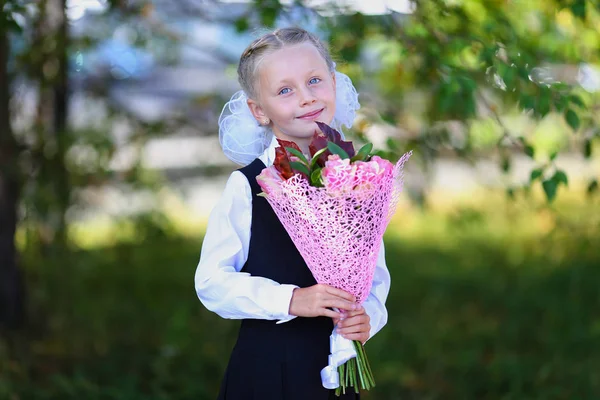 Portrait of a happy school girl in a uniform with bouquet of flowers. Back to school outdoors