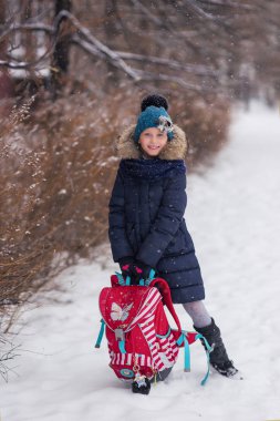 Okuldan sonra karlı bir parkta çantalı neşeli bir kız öğrenci.
