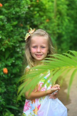 Gülümseyen küçük bir kızın portresi. Tropik yeşillik arka planda Kız.