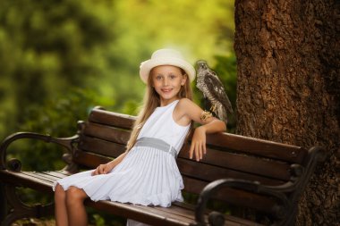 Omzunda bir kuş ile sevimli güzel kız bir park bankında oturuyor.