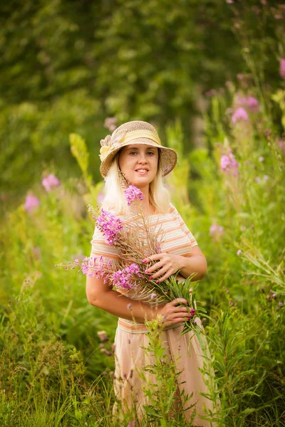 野生の花を持つかわいい笑顔のブロンドの女性 畑でバラ茶を飲む女性の夏の肖像 — ストック写真
