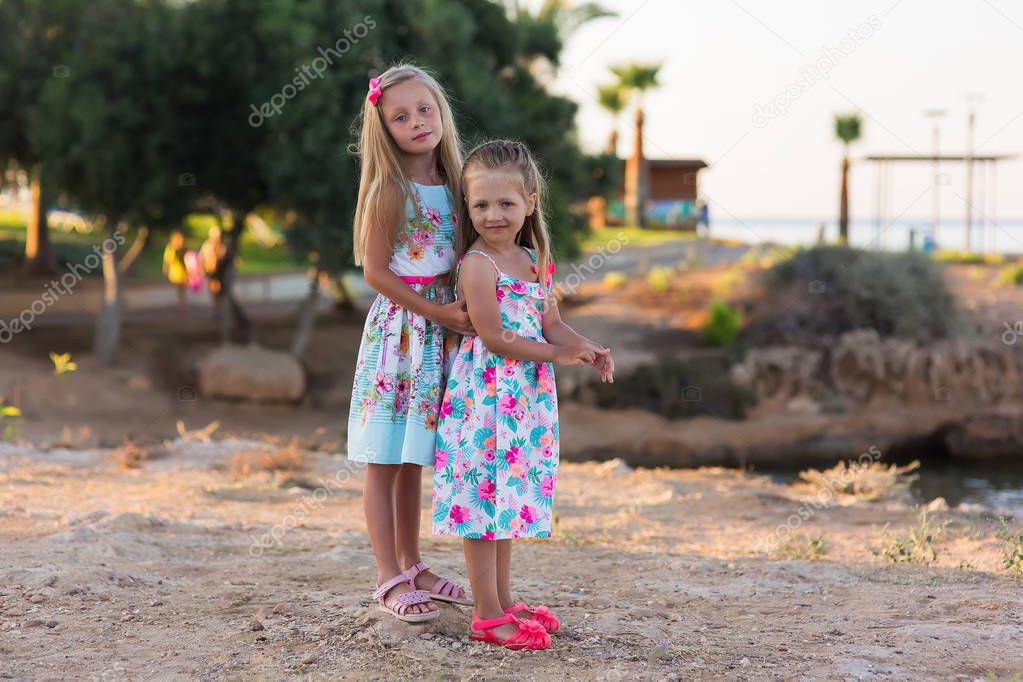 little happy girls on a walk on a summer evening at sunset in the park. Sisters