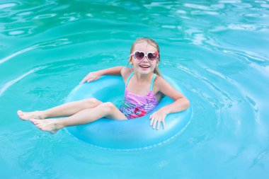 Güzel küçük kız havuzda yüzüyor ve şişme çemberle eğleniyor.