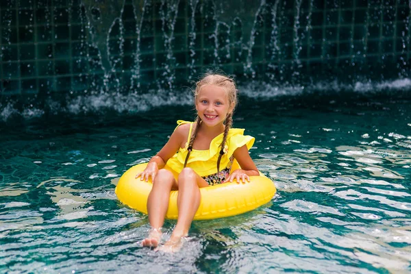 Güzel küçük kız havuzda yüzüyor ve şişme çemberle eğleniyor.