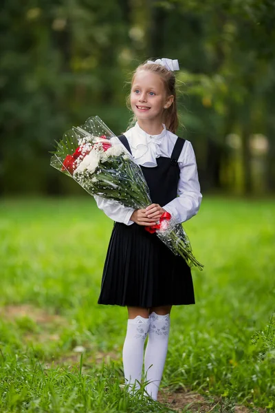 A girl child in school uniform goes to the school on September 1st. The girl is holding a bouquet of flowers. Close-up.