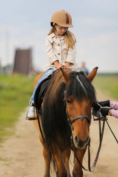 Little girl in an equestrian helmet riding a horse. Girl on a horse walk in nature.