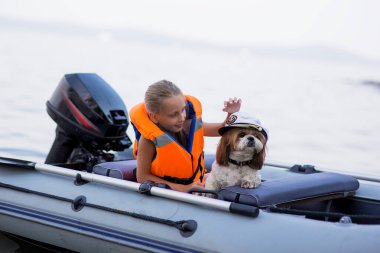Can yeleği giymiş küçük bir kız köpeğiyle gölde bir teknede. Güvenlik. Yaz tatili.