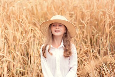 Buğday tarlasında mutlu bir çocuk. Beyaz saçlı güzel kız hasır şapkalı, olgun buğdaylı.