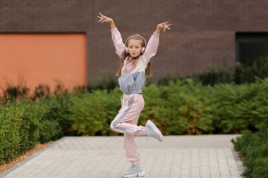 Mutlu sarışın kız kulaklıkla müzik dinliyor, sokakta dans ediyor..