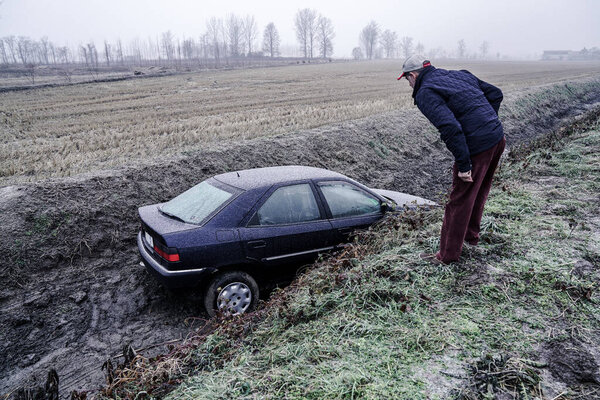 mortara - 01 / 13 / 2017: a passerby looks at a car that has fallen into a ditch because of the ice