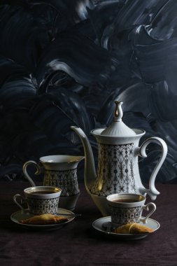 Kahve fincanı ve kahve. Masanın üstünde koyu keten masa örtüsü ve koyu arkaplanda kurabiyeler.