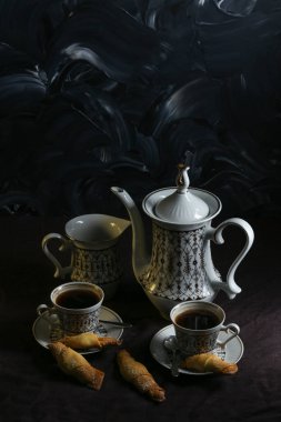 Kahve fincanı ve kahve. Masanın üstünde koyu keten masa örtüsü ve koyu arkaplanda kurabiyeler.