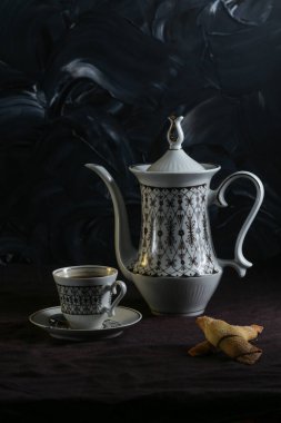 Kahve demliği ve fincanlar koyu arkaplanda koyu keten bir masa örtüsü olan bir masada.