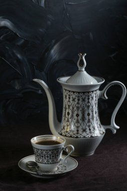 Kahve demliği ve fincanlar koyu arkaplanda koyu keten bir masa örtüsü olan bir masada.