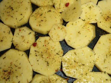 Bir tavada baharat ve otlarla birlikte çiğ patates dilimleri yakın plan..