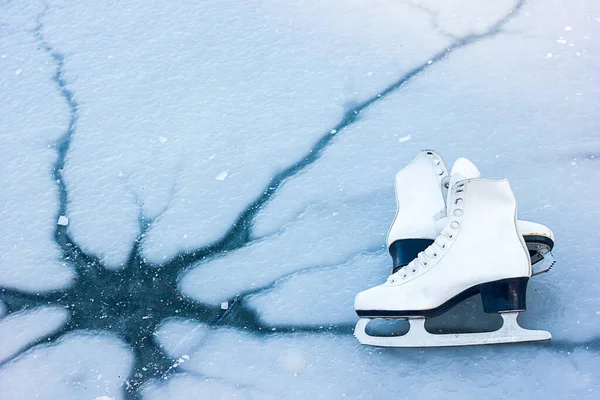 White figure skates lie on ice with a crack, cracked ice. The concept of the danger of being near a winter reservoir, space for text