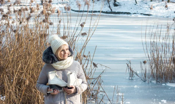 Kış kıyafetleri içinde bir kız ve donmuş bir gölün arka planında patenli bir şapka. Sağlıklı bir yaşam tarzı ve kışın açık hava aktiviteleri teması.