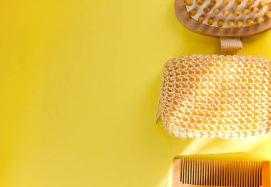 Doğal bez, ahşap masaj fırçası, sarı arka planda ahşap tarak, düz üst görünüm, ekoloji ve vücut bakımı için doğal malzemeler