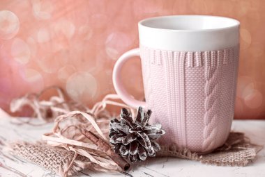 Güzel pembe kupa, örülmüş çam kozalağı ve bir çubuk vanilyalı arka planda pembe bir duvar, bokeh, ev konforu ve tatil.