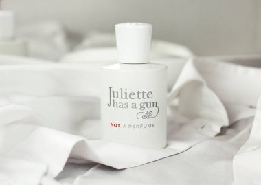 Beyaz parfüm şişesi Juliette 'in beyaz bir gömleğin arka planına dayanan bir silahı var. Temiz ve ferah bir parfüm kokusu.
