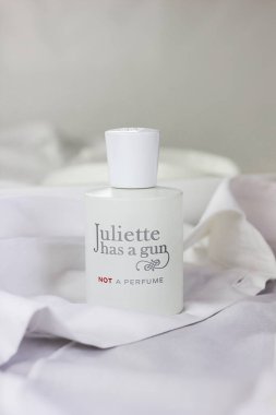 Beyaz parfüm şişesi Juliette 'in beyaz bir gömleğin arka planına dayanan bir silahı var. Temiz ve ferah bir parfüm kokusu.
